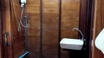A small, enclosed bathroom with a wooden door, a toilet, a sink, and a shower.