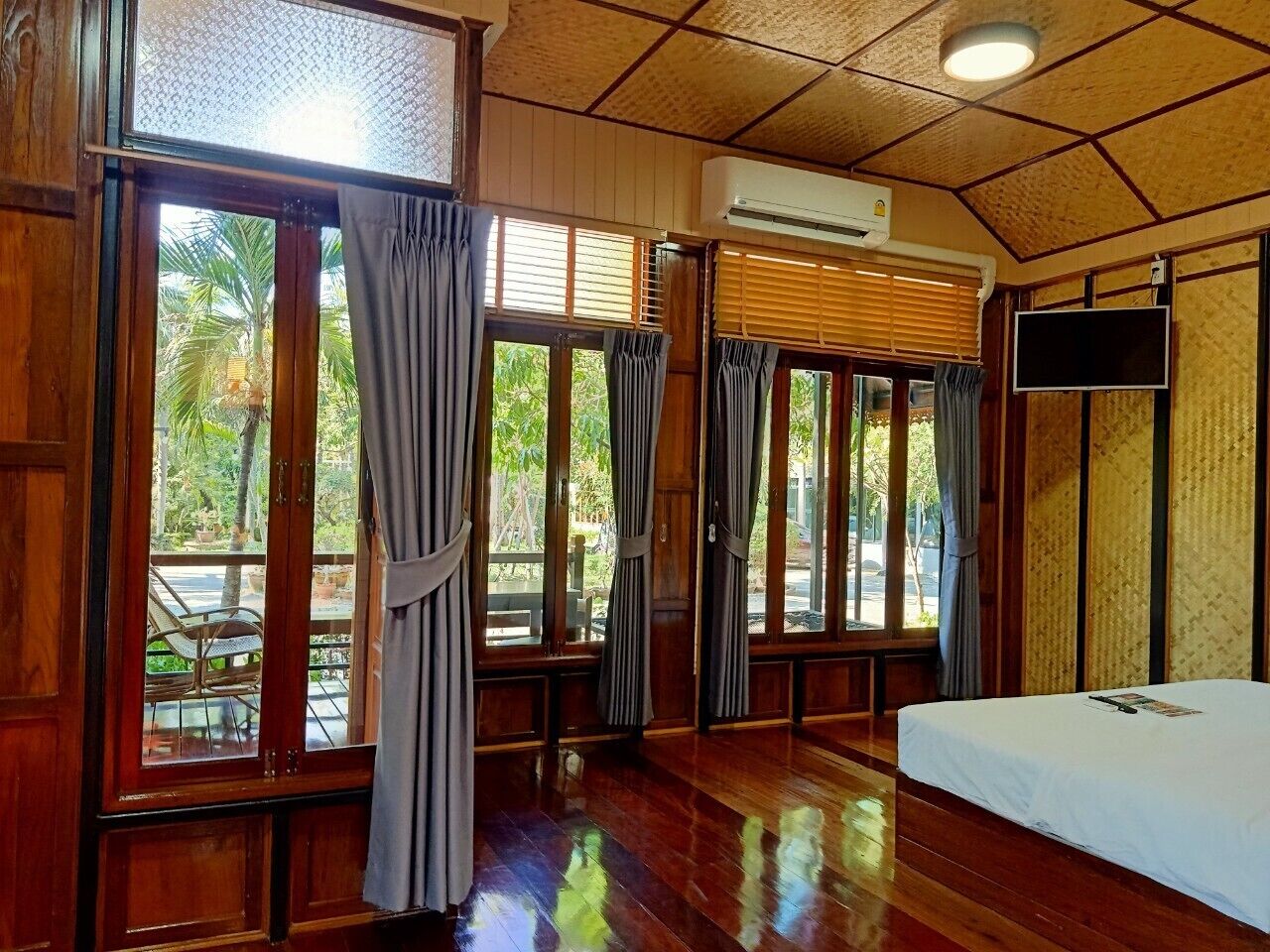 A room with a bed, large windows with curtains, a TV, and an air conditioning unit.