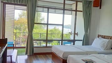 Une chambre d’hôtel avec deux lits, un plancher en bois, une grande fenêtre avec des rideaux et une vue sur la verdure.