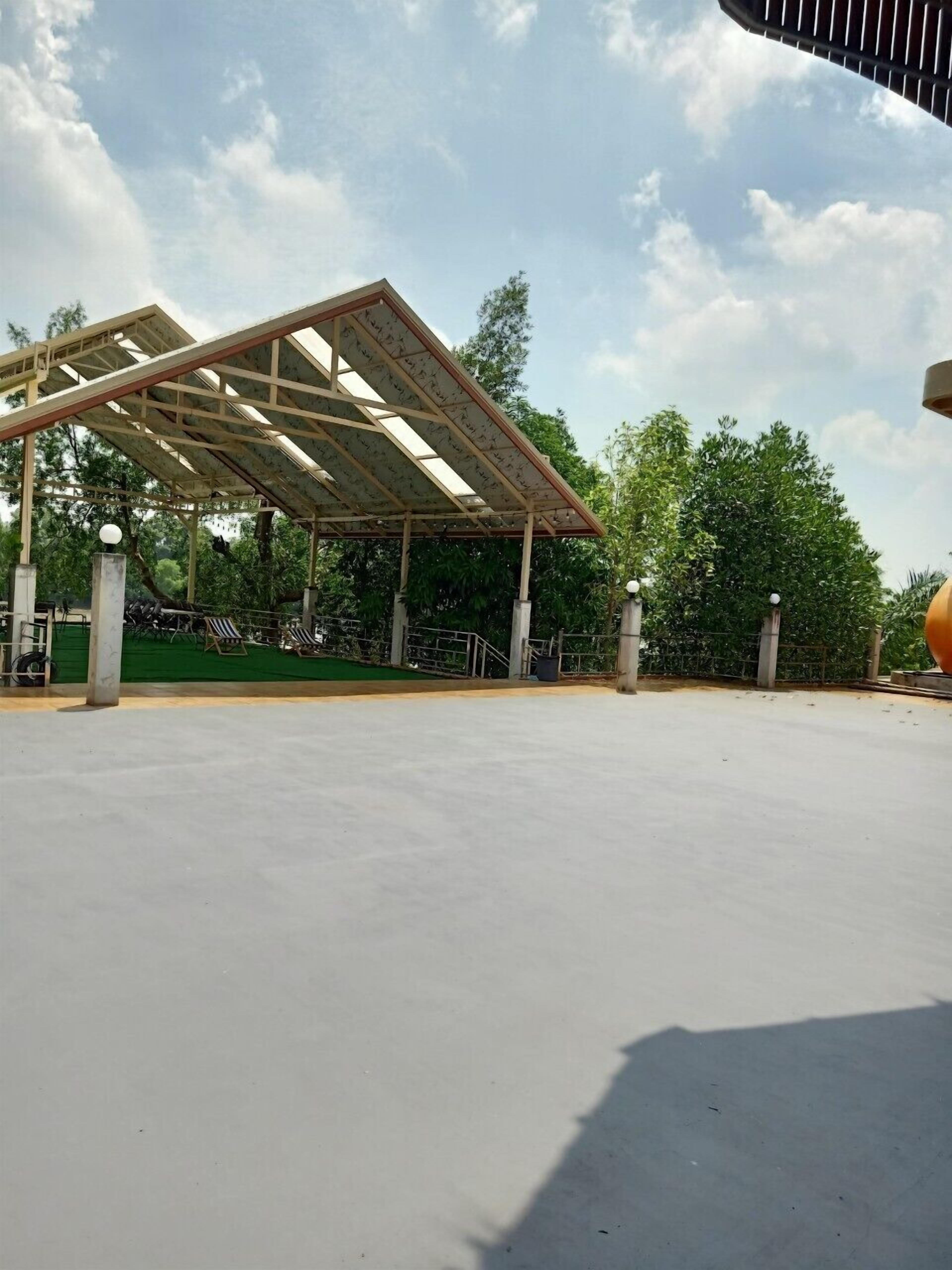 A covered outdoor area with a metal roof structure, concrete pillars, and a flat paved surface.