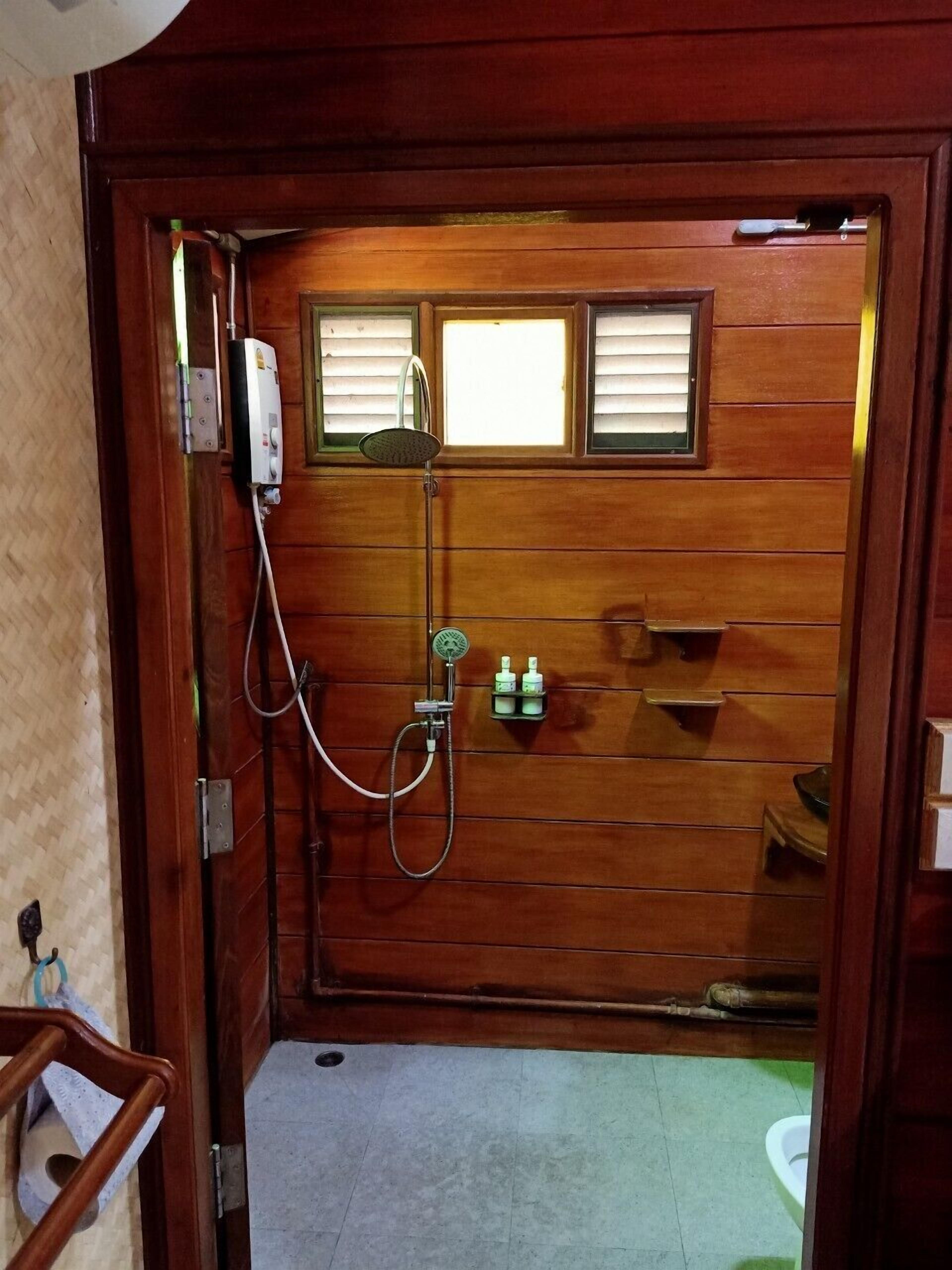 A wooden door with a shower, a small window, and a shelf with toiletries.
