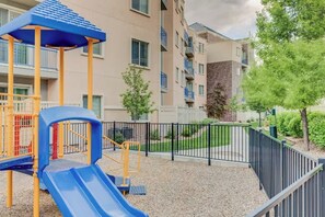 Un parque infantil con tobogán y estructuras de escalada, rodeado por una valla y edificios residenciales.