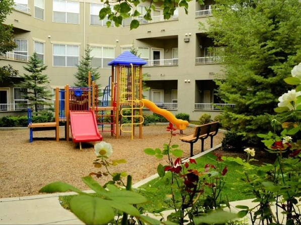 Un parque infantil con tobogán y estructuras de escalada, rodeado de grava y vegetación.