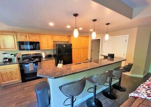 A modern kitchen with wooden cabinets, a black refrigerator, a stove, and a bar area with stools.
