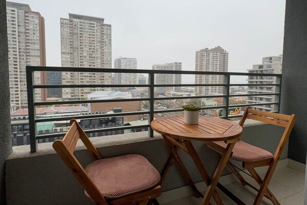 A balcony with a table and two chairs, overlooking a cityscape with high-rise buildings.