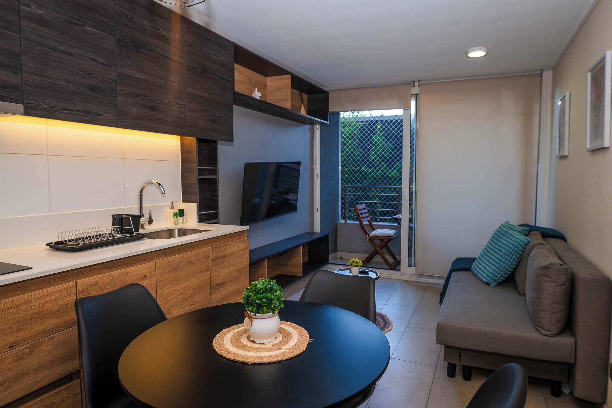 A modern kitchen with a dining area, a sofa, and a TV.