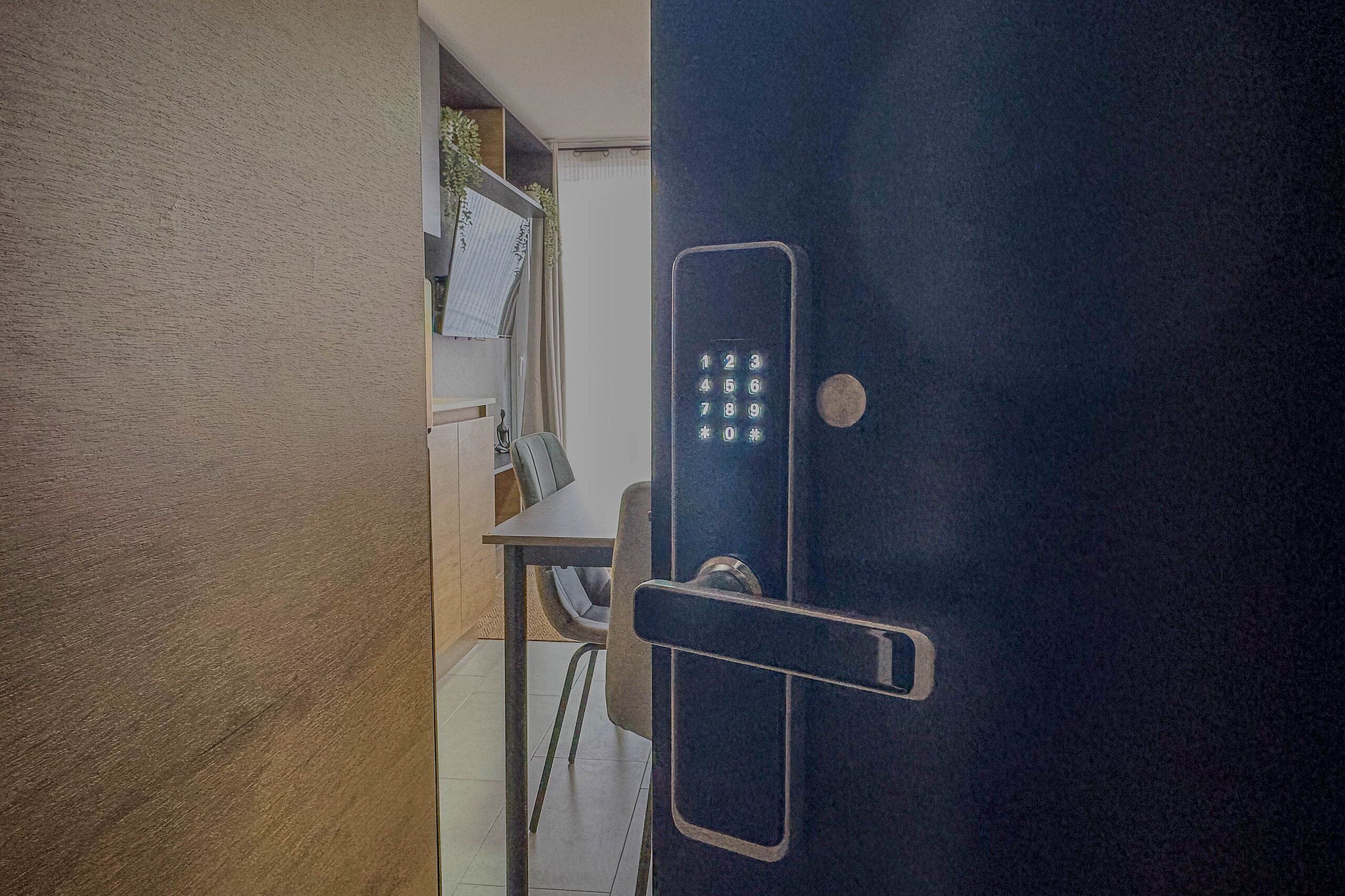 Una puerta con cerradura electrónica, una pequeña mesa y una silla al fondo.