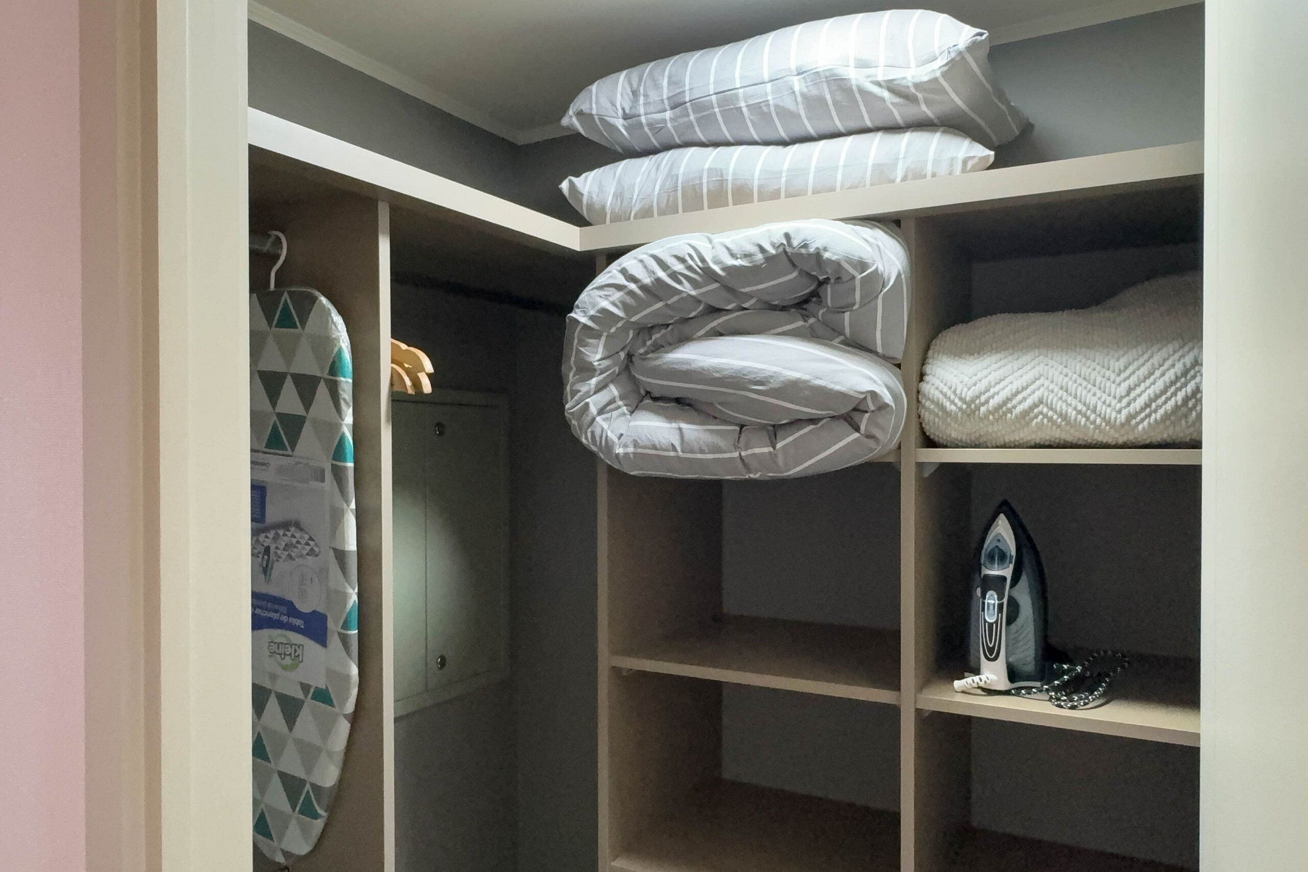 Un dormitorio con una cama litera, un tendedero y una estantería con un planchador.