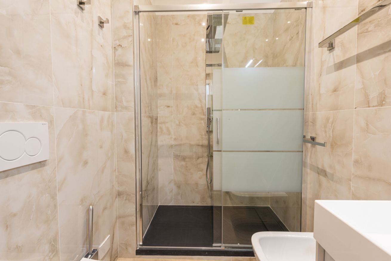 Un baño moderno con cabina de ducha de vidrio, un lavabo blanco y pared revestida de mármol.