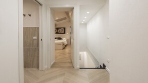 Un pasillo con piso de madera, una cama con cabecera blanca y un cuadro en la pared.