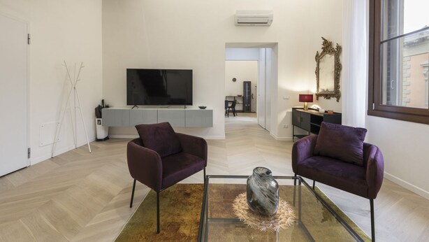Una sala de estar moderna con dos sillones morados, una mesa de centro de cristal, un televisor de pantalla plana grande y un diseño minimalista.
