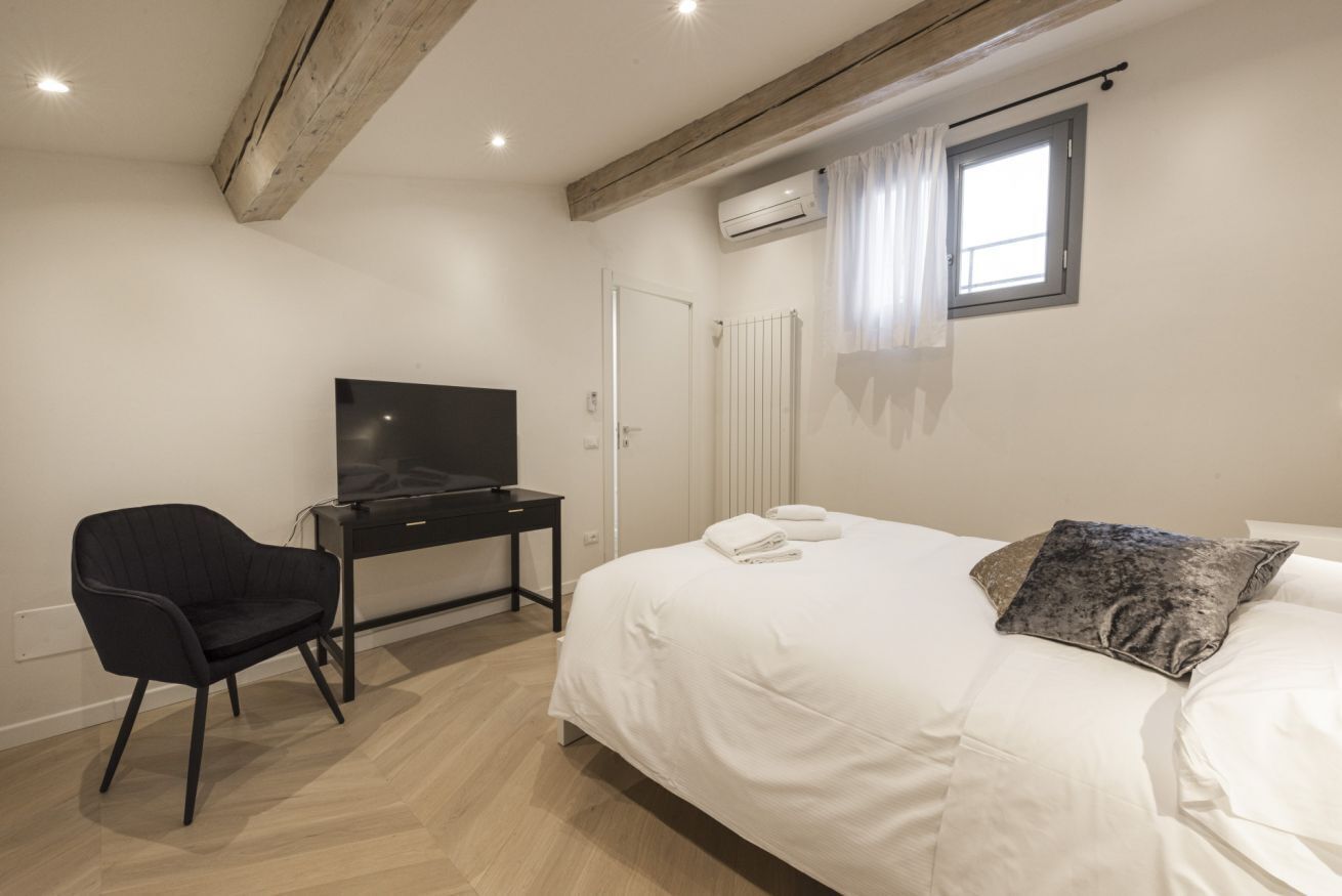 Une chambre à coucher avec un lit, un bureau avec une télévision, une chaise et une fenêtre avec des rideaux.