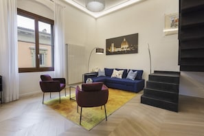 A modern living room with a blue sofa, two armchairs, a yellow rug, a staircase, and a cityscape painting. - Maison San Gallo by MMega (Firenze)