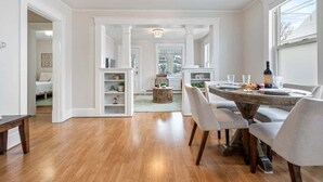 A spacious dining area with a round wooden table, white chairs, and a chandelier.