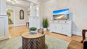 A living room with a round wooden coffee table, a white cabinet with a television, and a large window with a beach view.