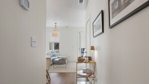 A hallway with a wooden floor, a white wall, a gold-framed mirror, and a small table with a lamp. -  Stylish Downtown Cottage w/ Golf Cart for Rent (Ocean Springs)