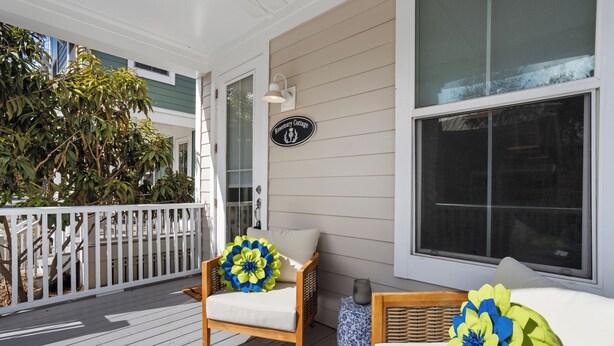 A wooden deck with a white railing, a chair with a blue and yellow flower pillow, and a sign reading "Rosemary Cottage." -  Stylish Downtown Cottage w/ Golf Cart for Rent (Ocean Springs)