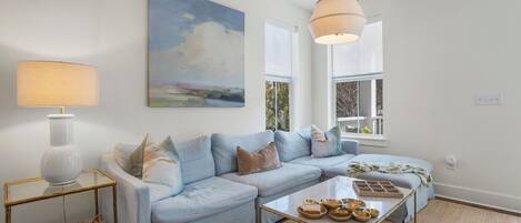 A living room with a light blue sofa, a glass coffee table, and a painting on the wall.