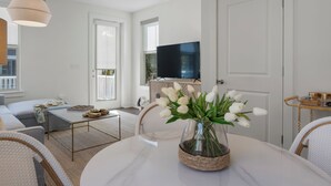 A modern living room with a white sofa, a coffee table, a TV, and a vase of white tulips. -  Stylish Downtown Cottage w/ Golf Cart for Rent (Ocean Springs)