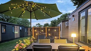 Eine Terrasse mit Tisch, Stühlen, einem grünen Sonnenschirm und Lichterketten.