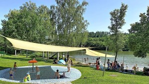 Ein Park mit einem Wasserspielplatz, einer überdachten Sitzgelegenheit und einem See.