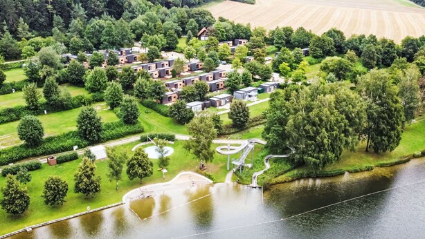 Eine Luftaufnahme eines Seeanwesens mit mehreren Ferienhäusern, einem gewundenen Weg und einer kreisförmigen Wasserspiele.