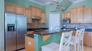Una cocina con armarios de madera, un refrigerador de acero inoxidable, un microondas y una isla grande con taburetes de bar.