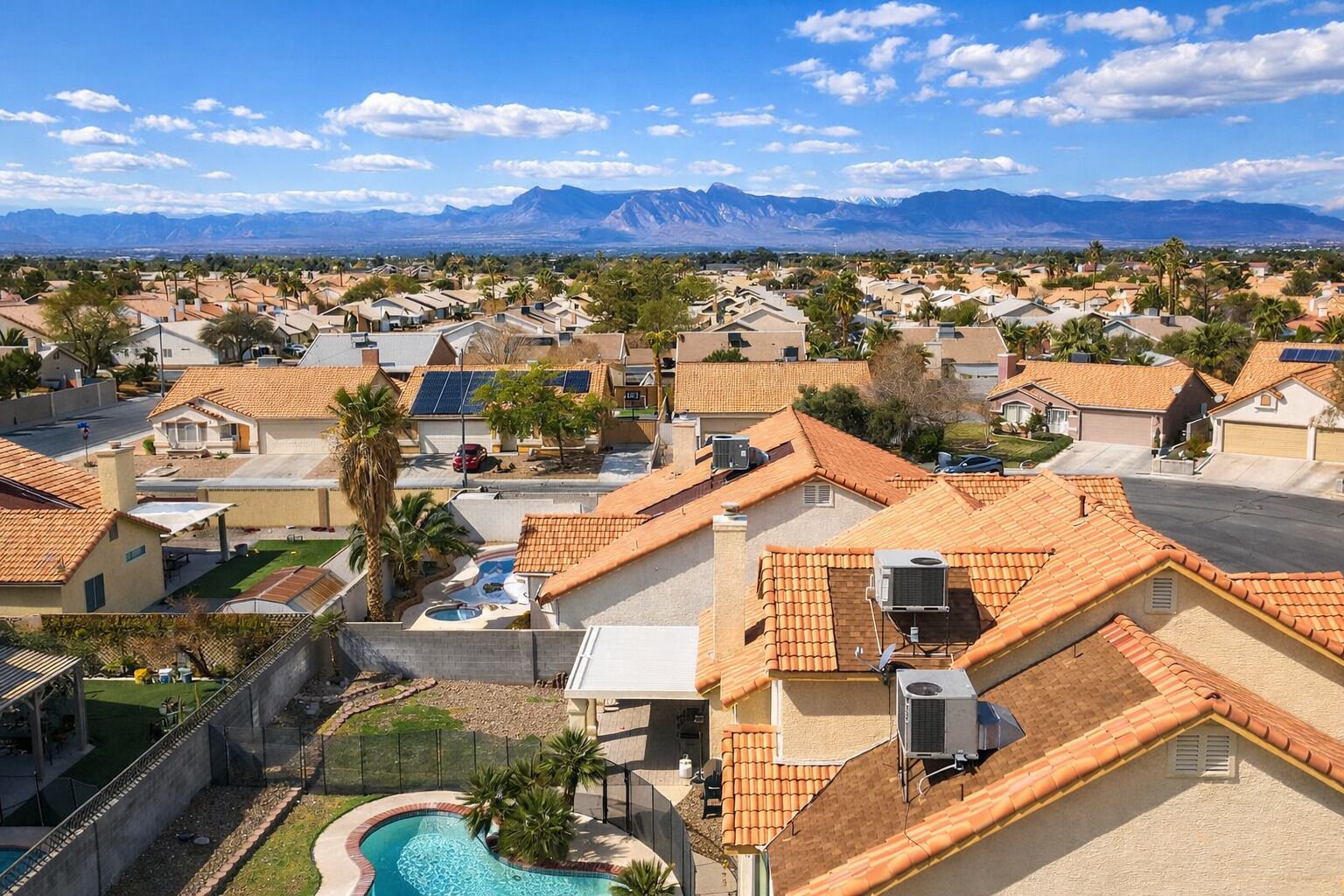 Zona residencial com casas, piscina e montanhas ao fundo.