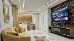 Ein modernes Wohnzimmer mit einer Couch, einem Couchtisch, einem an einer Marmorwand montierten Fernseher und einer Küche im Hintergrund.