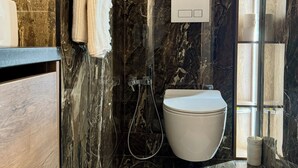 Ein modernes Badezimmer mit Marmorwand, Toilette, Dusche und Handtuchhalter.