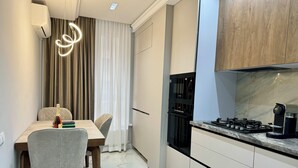 Eine moderne Küche mit Einbauherd, Backofen und Mikrowelle. Ein Essbereich mit Tisch und Stühlen lädt zum Verweilen ein, und ein Vorhang trennt Küche von Wohnbereich.