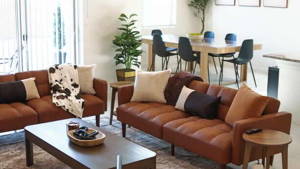 Un salon avec deux canapés marron, une table basse et un coin repas comprenant une table et des chaises.