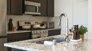 Une cuisine avec des meubles de couleur sombre, un four à micro-ondes en acier inoxydable, une cuisinière à gaz et un plan de travail en granit.