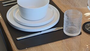 Une table à manger dressée avec des bols, des assiettes et des verres blancs, et un saladier rempli de verdure au centre.