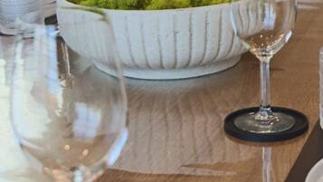 Una mesa de comedor con un bol blanco de musgo verde, dos copas de vino y un extintor de incendios al fondo.