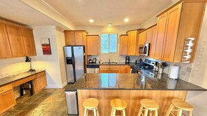Eine moderne Küche mit Holzschränken, einem Edelstahlkühlschrank, einer Granit Arbeitsplatte und drei hölzernen Barhocker.