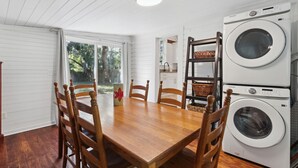 Uma sala de jantar com mesa e cadeiras de madeira, máquina de lavar e vista para o exterior.