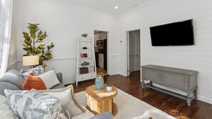 Uma sala de estar com ventilador de teto, televisão na parede, mesa de centro de madeira e estante de livros.