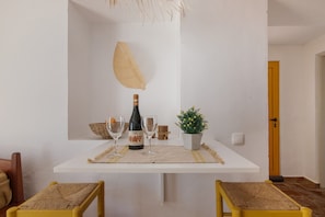 A dining area with a white table, yellow chairs, a bottle of wine, two wine glasses, a small plant, and a hanging light fixture.