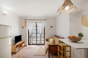 A modern living room with a TV, sofa, dining table, and a large window with curtains.