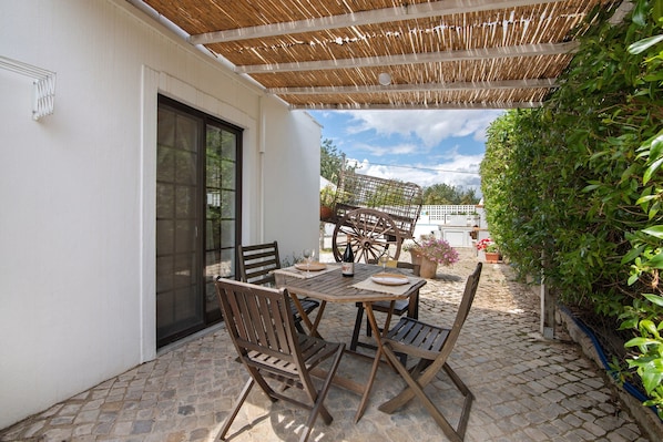 An outdoor patio with a table and chairs, a wooden pergola, and a view of the garden.