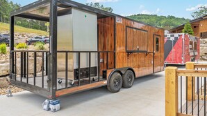 Un remolque móvil con estructura metálica, revestimiento de madera y un espacio cerrado pequeño con una ventana.