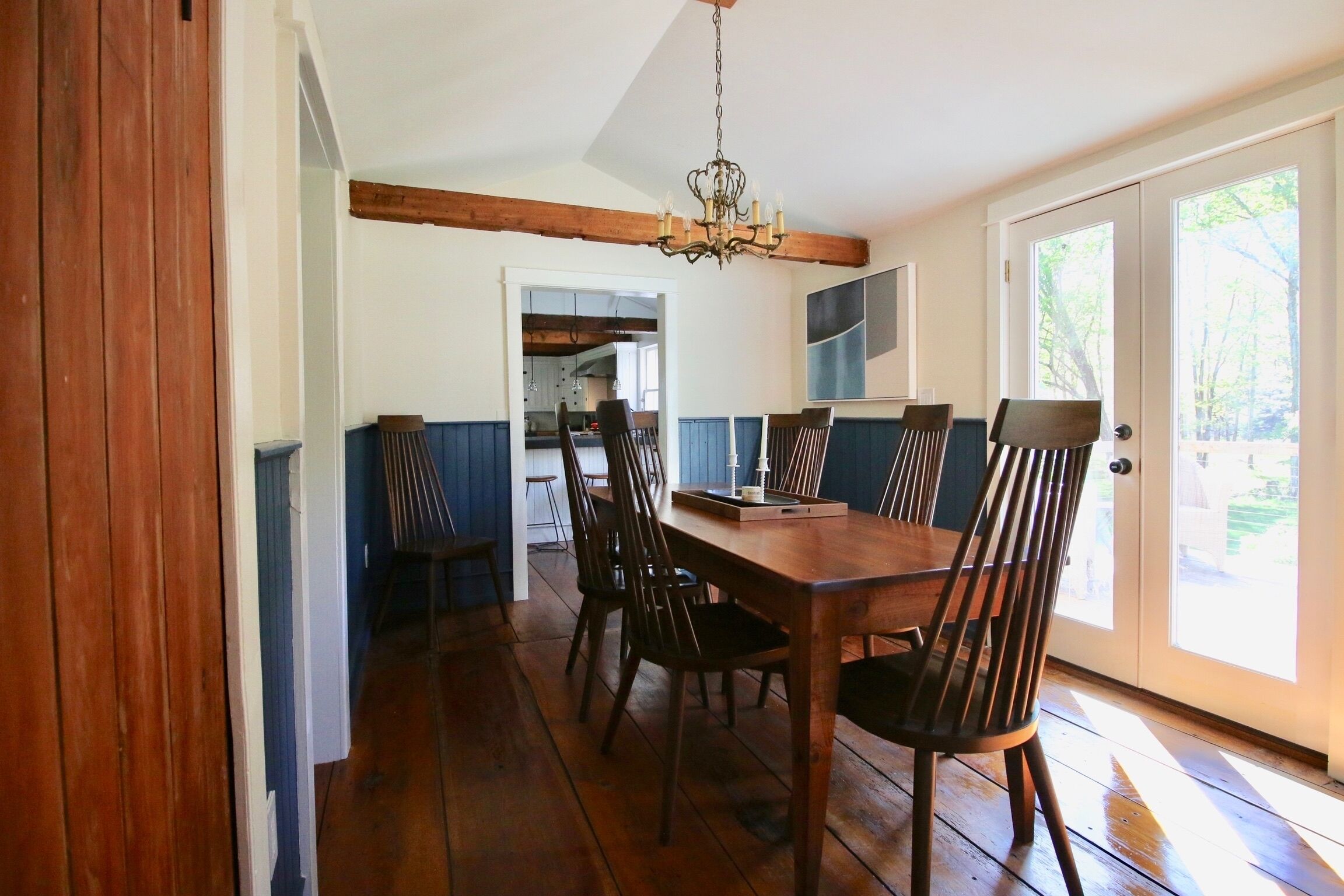 A dining area with a wooden table and chairs, a chandelier, and a view through a glass door.