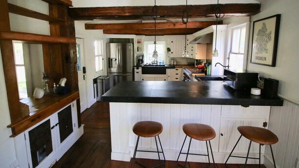 Una cocina con una isla grande, vigas de madera, armarios blancos y taburetes de bar.