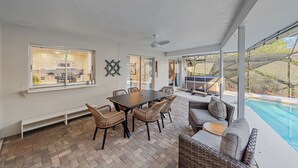 A covered patio area with a dining table and chairs, a sofa, and a view of a swimming pool. - Breezemont Bungalow | Private Heated Pool, Hot tub + Sauna (Sarasota)