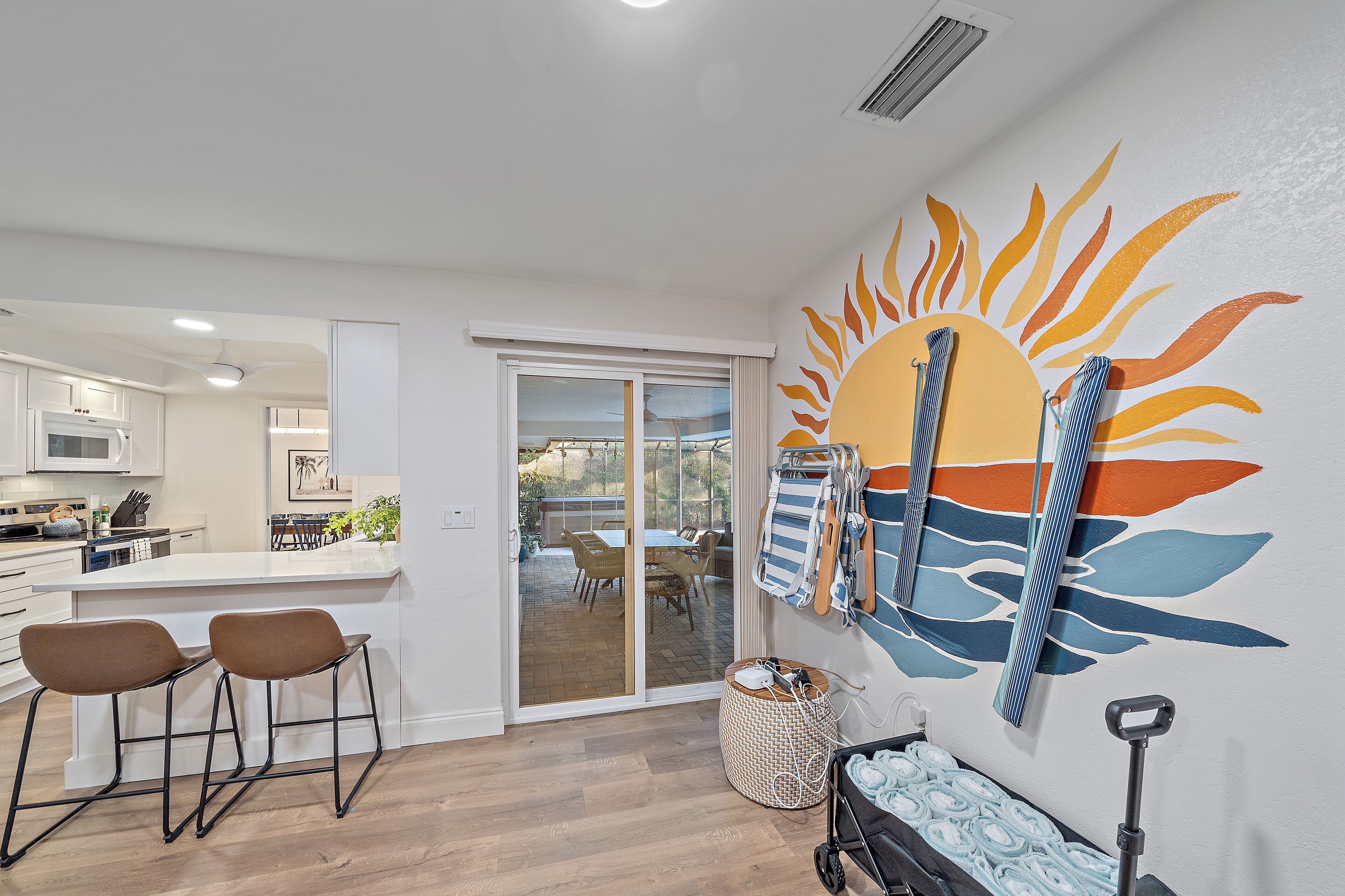 Una cocina moderna con armarios blancos, un área de comedor con mesa y sillas, y un mural de sol en la pared.