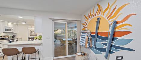 Una cocina moderna con armarios blancos, un área de comedor con mesa y sillas, y un mural de sol en la pared.