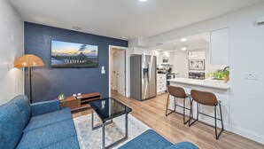 A modern living room with a sofa, a glass coffee table, and a TV mounted on the wall. - Breezemont Bungalow | Private Heated Pool, Hot tub + Sauna (Sarasota)
