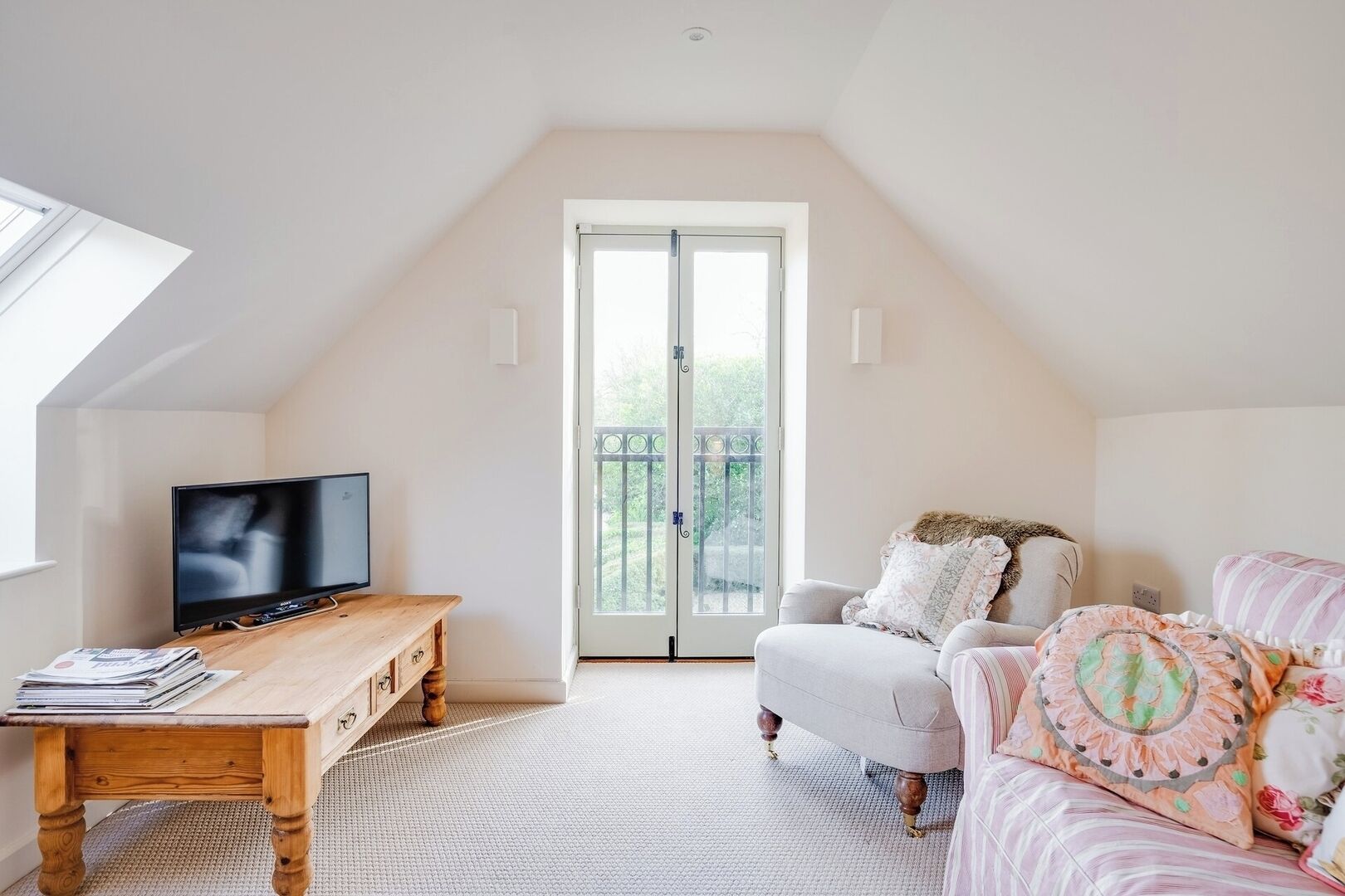 A cozy loft bedroom with a wooden desk, a television, a cushioned sofa, and a large sliding glass door leading to a balcony.