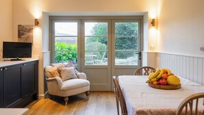 Une pièce confortable avec un canapé, une table à manger ornée de fruits, un téléviseur et une porte donnant sur un jardin.